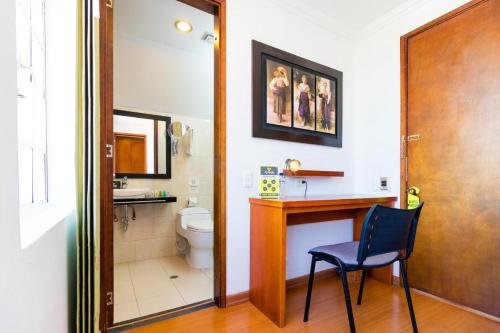 a bathroom with a toilet and a desk and a chair at ApartaSuites & Hotel Bogota Plaza 36 in Bogotá