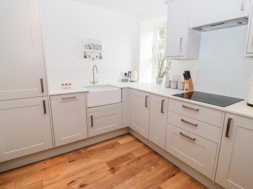 a white kitchen with white cabinets and a wooden floor at Sarah's Cottage in Morpeth