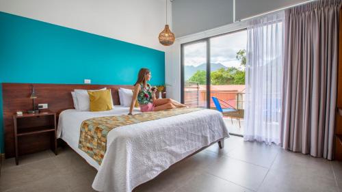 uma mulher sentada numa cama num quarto de hotel em La Fortuna Lodge by Treebu Hotels em La Fortuna