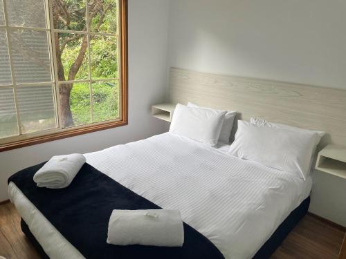 a bedroom with a large white bed with a window at Cumberland River Holiday Park in Lorne