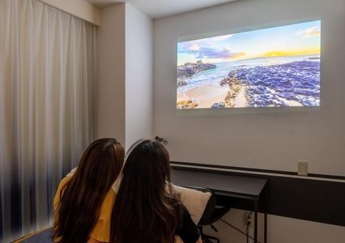 two women sitting in a room watching a presentation at Hotel Graphy Nezu in Tokyo