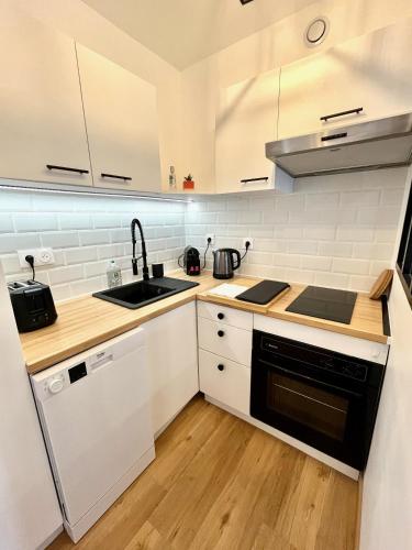 une cuisine avec des armoires blanches, un évier et une cuisinière dans l'établissement Studio avec grande terrasse et parking privatifs, à Caen