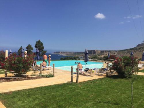 a group of people sitting around a swimming pool at Central Apartment Macari Cala Azzurra Residence in Macari