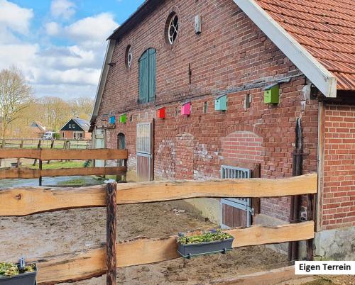 a brick barn with a wooden fence in front of it at De Varkensstal in De Heurne