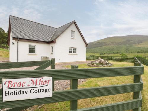 a white house behind a fence with a large mirror holiday cottage at Brae Mhor Cottage in Fort William
