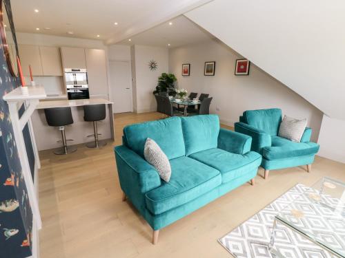 a living room with two blue couches and a kitchen at 21 The Rest in Porthcawl