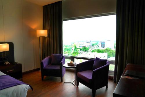 a hotel room with a bed and two chairs and a window at Indigo Heights Hotel & Suites in Lahore