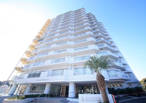 a tall white building with a palm tree in front of it at Katsuura Hilltop Hotel & Residence in Katsuura
