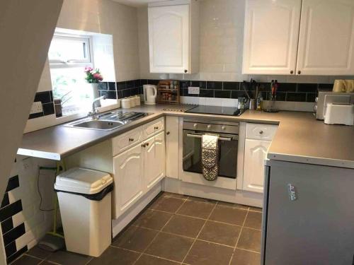 uma cozinha com armários brancos e um lavatório em Corner Cottage - base for exploring North Norfolk em Bodham