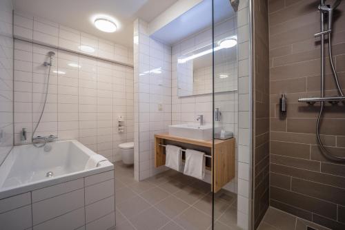 een badkamer met een bad, een wastafel en een douche bij Fletcher Hotel-Restaurant Leidschendam – Den Haag in Leidschendam