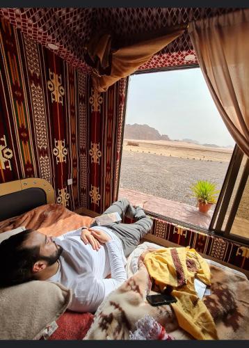 a man laying on a bed in a room with a window at Shakria Bedouin Life Camp in Wadi Rum