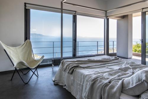 ein Schlafzimmer mit einem Bett und einem Stuhl sowie großen Fenstern in der Unterkunft Seaview Villa Schinias in Schinias