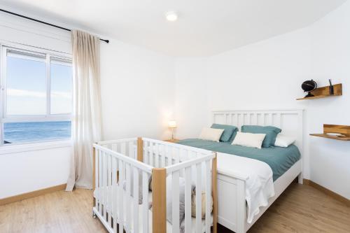 biała sypialnia z łóżeczkiem dziecięcym i oknem w obiekcie Home2Book Comfy Beachfront Radazul w mieście Radazul