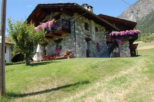 a stone house with a balcony and flowers on it at Aparthotel Foyer d'antan SUITE con caminetto hammam o vasca idromassaggio in Brusson