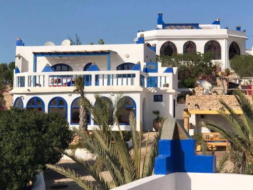 a white and blue house with palm trees in front of it at Room in villa Lair De La Mer in Sidi Kaouki