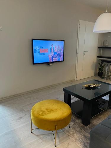 a living room with a table and a yellow stool and a tv at Cosy Apartment on an amazing location! in Skopje