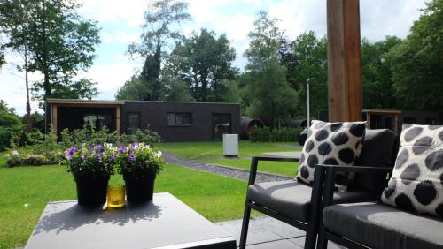 een patio met 2 stoelen en een tafel met bloemen erop bij The Black Oak - Luxe bungalow met prive sauna in Voorthuizen