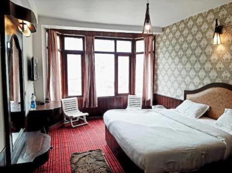a bedroom with two beds and a desk and windows at vella Mrina Group of hotel Manali in Manāli