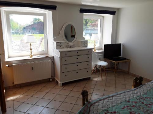 a bedroom with a dresser and a mirror and two windows at Ferienwohnung im Palais Rosenlund in Hürup