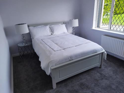 a bedroom with a white bed with two lamps and a window at 4 Bedroom, 15 min to Limerick city Quiet Retreat. in Limerick