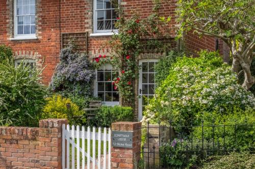 a brick house with a white fence and flowers at Adorable cottage with a log burner in heavenly village - Constable Lodge in Nayland