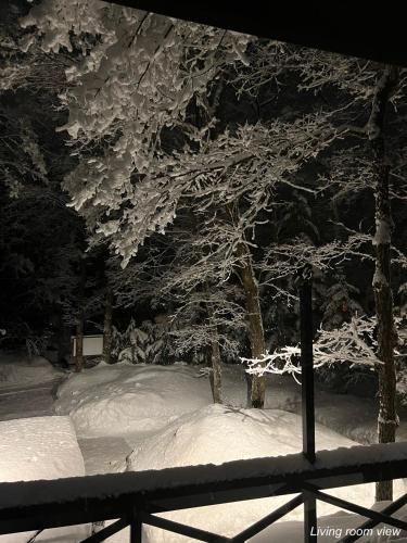 a tree covered in snow next to a fence at The Guest House Japan Hakuba in Hakuba
