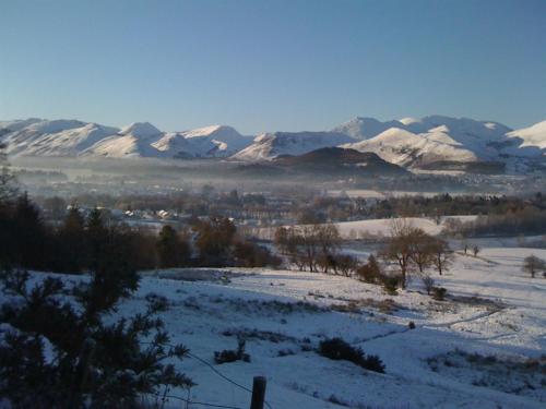 a snowy field with snow covered mountains in the background at Woodside Bed and Breakfast in Keswick