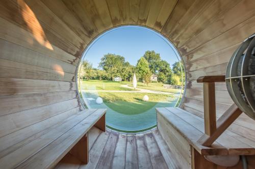 - une fenêtre ronde dans un sauna avec vue sur la cour dans l'établissement Maisons d'hôtes - Domaine Le Coq Enchanté, à Cambremer