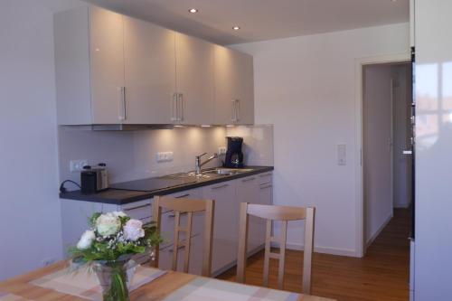 a kitchen with white cabinets and a table with a vase of flowers at Ferienwohnung Rosenberger in Kolitzheim