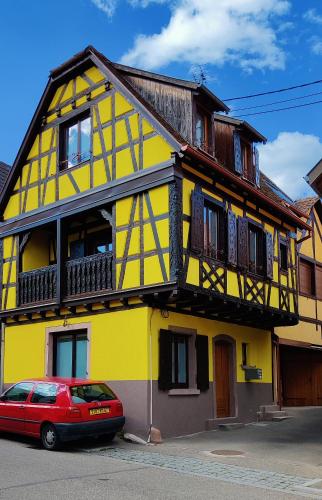 une maison jaune avec une voiture rouge garée devant elle dans l'établissement La Maison Alsacienne, à Kintzheim