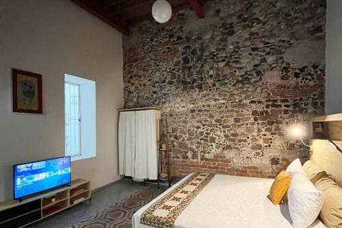 a bedroom with a brick wall with a bed and a television at 107 SUITES DONCELES CENTRO HISTÓRICO CDMX in Mexico City