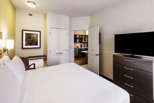 a bedroom with a white bed and a flat screen tv at Candlewood Suites Lenexa - Overland Park Area by IHG in Lenexa