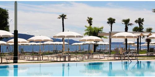 a swimming pool with umbrellas and tables and chairs at Hotel Du Lac Gardone Riviera in Gardone Riviera
