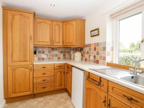 een keuken met houten kasten, een wastafel en een raam bij Wellfield Cottage in Highbridge