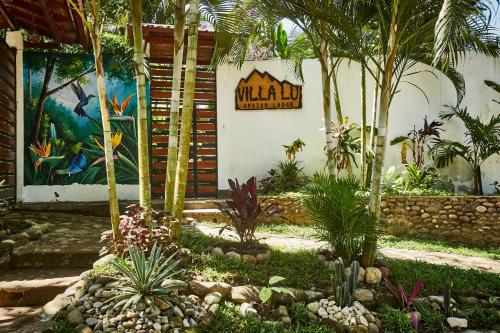 a garden with palm trees and a sign on a building at Villa Lu Amazon Ecolodge in Tarapoto