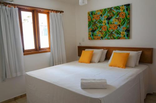 ein Schlafzimmer mit einem großen weißen Bett mit orangefarbenen Kissen in der Unterkunft Res Village do Bosque 16 in Porto Seguro