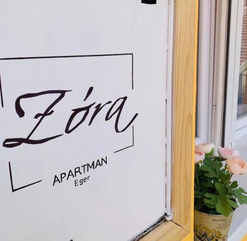a sign on a window with flowers in a vase at ZÓRA APARTMAN in Eger