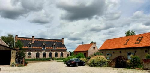 une voiture noire garée dans un parking entre deux bâtiments dans l'établissement Paardenhof Guesthouse, à Esquelbecq