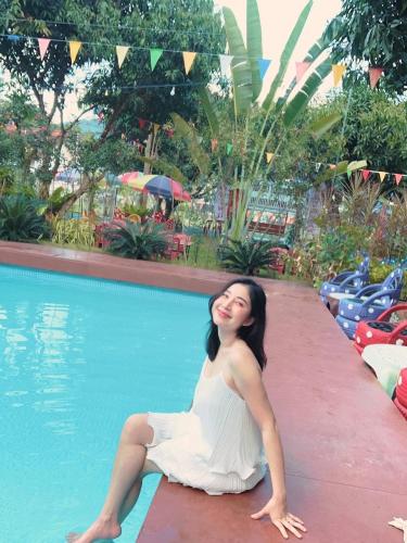 a woman in a white dress sitting next to a swimming pool at บ้านเดอะเมาเท่น By The Mountain Ozoneบ้านโอโซนขุนเขาแก่งกระจาน in Ban Song Phi Nong