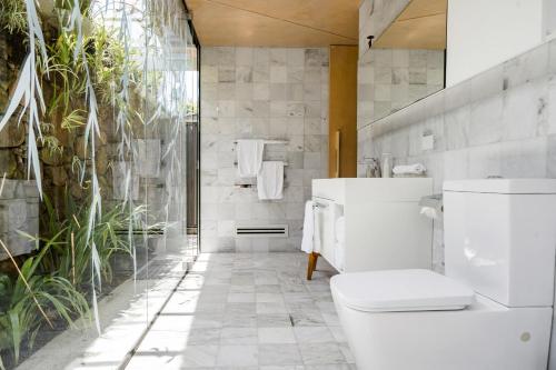 a white bathroom with a toilet and plants at Buhwi Bira Byron Bay - Studio in Byron Bay