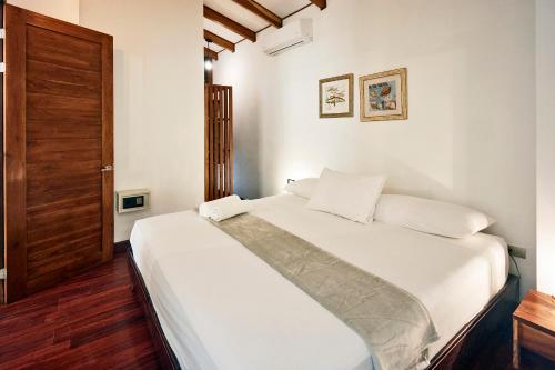 1 dormitorio con cama con sábanas blancas y puerta de madera en Casas Santa Teresa, en Santa Teresa Beach