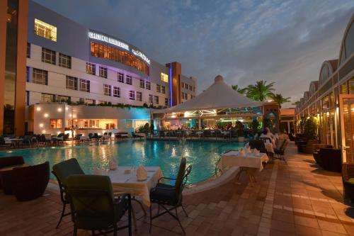 a swimming pool with tables and chairs in front of a hotel at Carlton Al Moaibed Hotel in Dammam