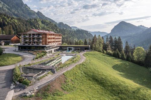 un grand bâtiment sur une colline à côté d'une rivière dans l'établissement Ruhehotel & Naturresort Rehbach - Adults only, à Schattwald