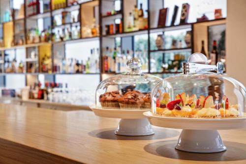 Dos pasteles y tartas en recipientes de cristal sobre un mostrador. en IntercityHotel Dortmund, en Dortmund