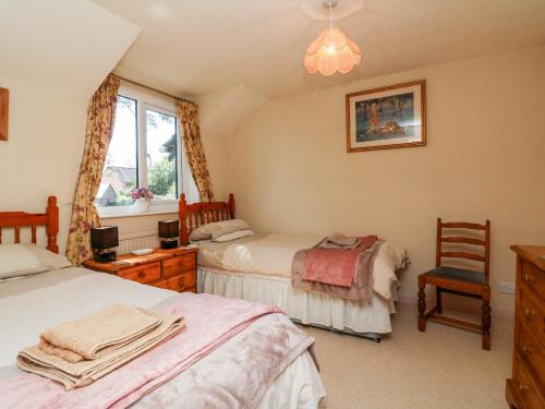 a bedroom with two beds and a chair and a window at Ash Tree Cottage in Holsworthy