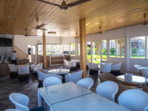 a restaurant with white tables and chairs and windows at Maargit Beach Resort in Mandrem