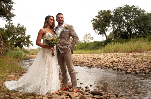 a bride and groom standing next to a stream at Karongwe - River Safari Lodge in Hoedspruit