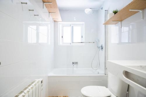 La salle de bains blanche est pourvue de toilettes et d'une baignoire. dans l'établissement Montjuic1, à Barcelone