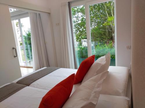 a white bed with red pillows in front of a window at Píllaras da Lanzada in A Lanzada