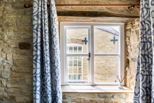 una ventana con cortinas azules y blancas en una pared de piedra en Windsor Cottage - Bolthole in the heart of CN!, en Chipping Norton